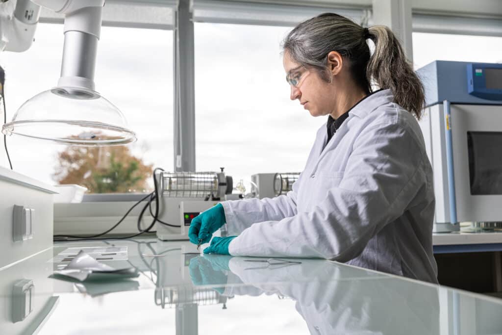 Laboratory technician working with protective gloves at a research workstation surrounded by scientific equipment