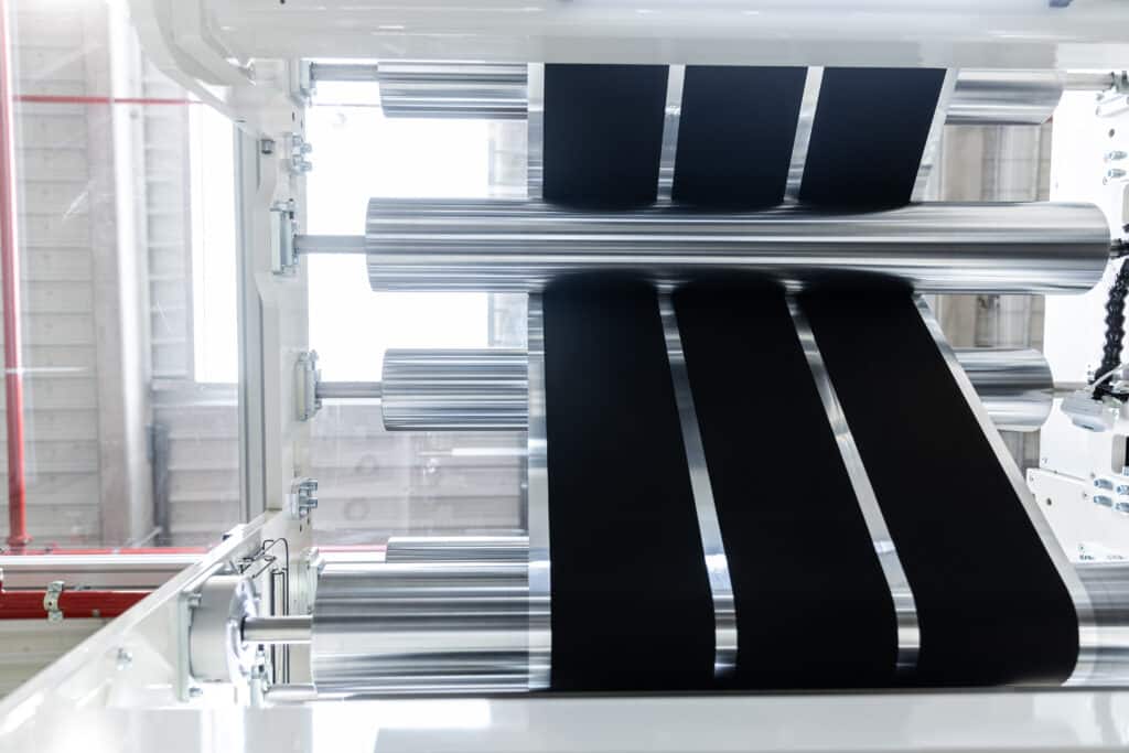 Industrial machine processing black coated foil through multiple polished metal rollers